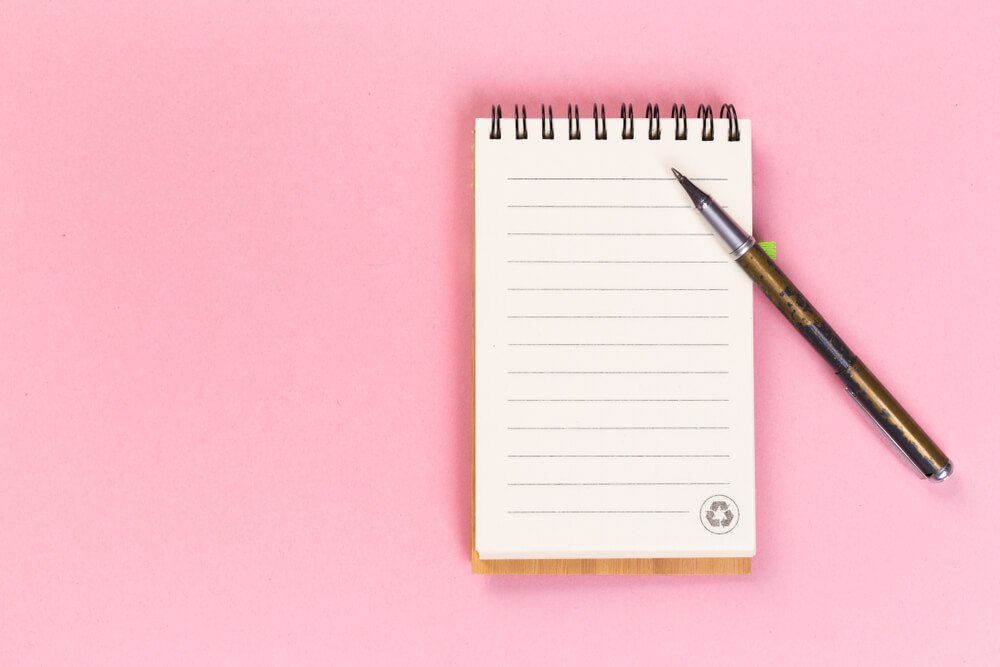 ピンクの背景に並べられたノートとペン.jpg